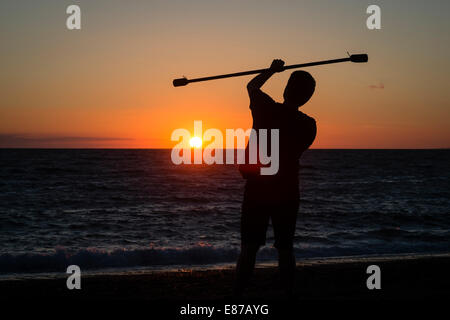 Serata estiva: un uomo in silhouette praticare la giocoleria circus competenze con fuoco spento bar al tramonto sulla spiaggia di Aberystwyth, Galles Foto Stock