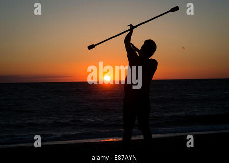 Serata estiva: un uomo in silhouette praticare la giocoleria circus competenze con fuoco spento bar al tramonto sulla spiaggia di Aberystwyth, Galles Foto Stock