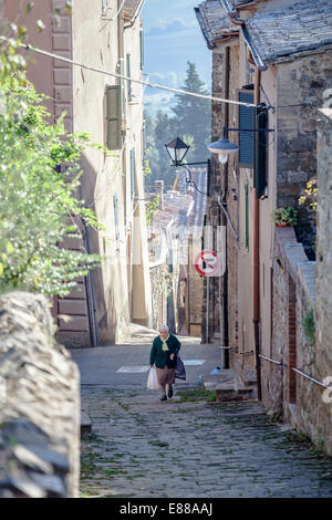 Vecchia donna triste portante due borse nella strada stretta in Montalcino Italia Toscana Foto Stock