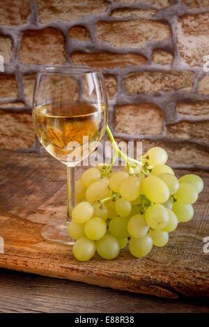 Bicchiere di vino bianco con uve sul tavolo di legno Foto Stock