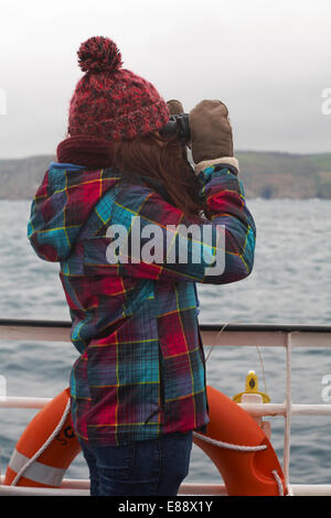 Giovane donna guardando attraverso il binocolo a bordo della RMV Scillonian III voce per le isole Scilly, Scillies, Cornwall nel mese di aprile Foto Stock