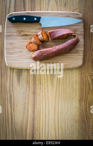 Il salame chorizo tagliato a pezzi su un tagliere di legno con coltello accanto ad essa. Foto Stock