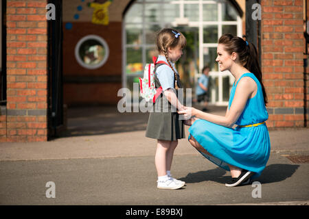 Un attraente, sorridendo felice giovane mamma consolante e di prelevare o far cadere la figlia presso la scuola infantile gates Foto Stock