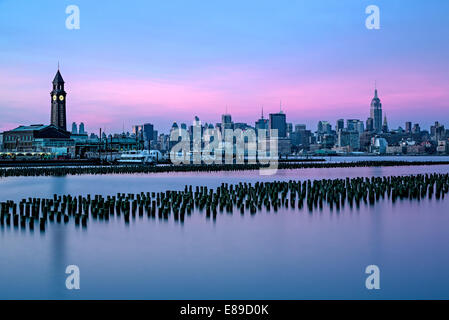 Sullo skyline di New York insieme a Empire State Building illuminato e la Erie Lackawanna terminale in Hoboken, New Jersey. Foto Stock