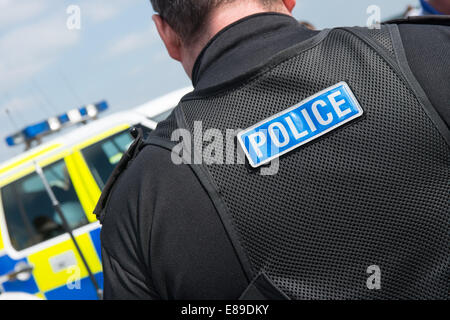 Un caucasico maschio britannico poliziotto che indossa la polizia moderna uniforme con la polizia di parola cucita sul retro del suo gilet tattico Foto Stock