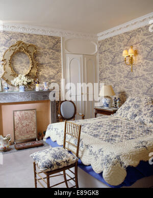 Blu Toile de Jouy carta da parati in camera da letto con motivi floreali blu trapuntato sul letto e ornato cornice immagine sopra il camino Foto Stock