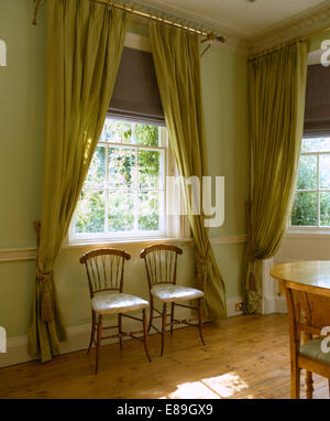 Biancheria tende e tendaggi verde sulla finestra sopra semplici sedie in verde pallido camera da letto con pavimento in legno Foto Stock