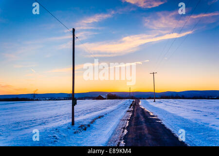 Tramonto sulla strada di un paese attraverso la coperta di neve i campi nelle zone rurali Frederick County, Maryland. Foto Stock