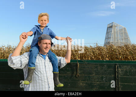 Padre che porta il suo figlio sulle spalle in cornfield, Stazione Elettrica Geotermica in background, Baviera, Germania Foto Stock