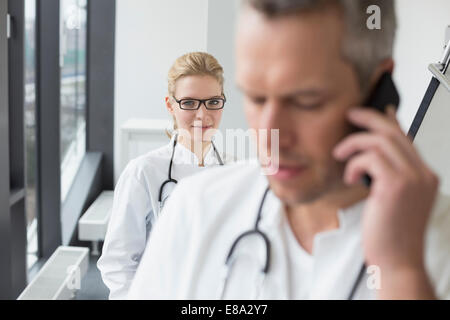 Medico sul telefono mentre medico donna in background Foto Stock