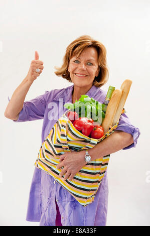 Donna senior con verdura shopping bag e mostra Thumbs up, sorridente, ritratto Foto Stock