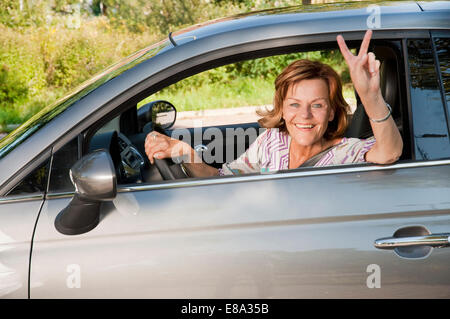 Senior donna seduta in auto e mostrando segno di vittoria Foto Stock