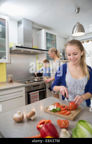 Figlia di verdure di taglio mentre la madre con figlio in background Foto Stock