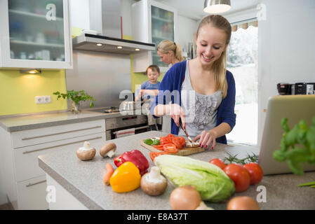 Figlia di verdure di taglio mentre la madre con figlio in background Foto Stock