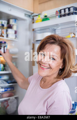 Ritratto di donna senior infront di aprire frigorifero, sorridente Foto Stock