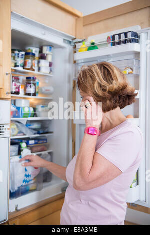 Senior donna infront di aprire frigorifero, sorridente Foto Stock