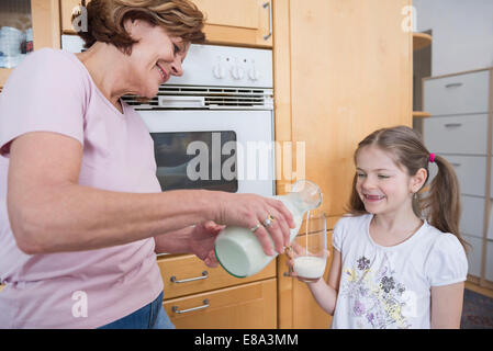 Nonna versando il latte in vetro per la nipote Foto Stock