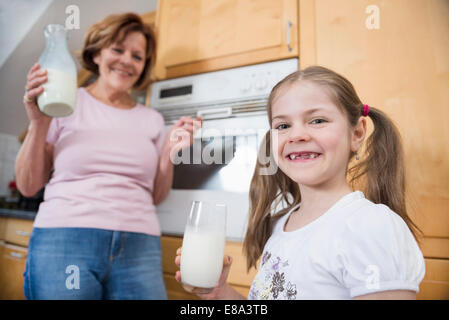 Nonna e nipote tenendo un bicchiere di latte, sorridente Foto Stock