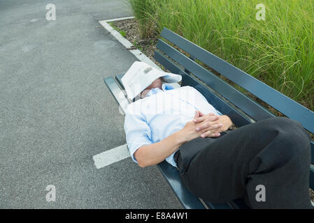 L'uomo coperto con il giornale è dormire su un banco di lavoro Foto Stock