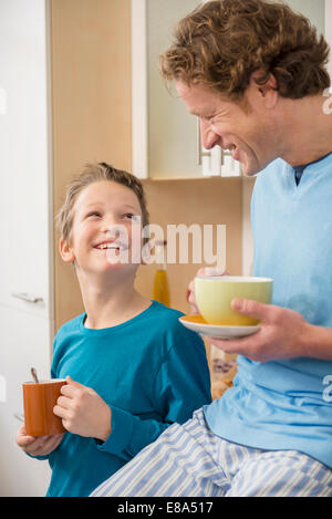 Sorridente padre e figlio con coppe in cucina Foto Stock