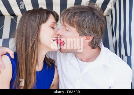 Accoppiare la condivisione di fragola dal tetto in vimini sedia spiaggia, sorridente Foto Stock