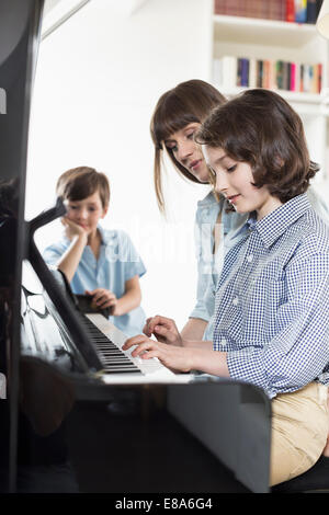 Madre e figlia suonare il pianoforte mentre il fratello in ascolto Foto Stock