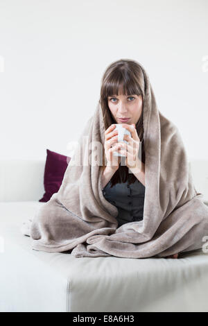 Ritratto di metà donna adulta coperto con coperta e un bicchiere di contenimento del tè Foto Stock