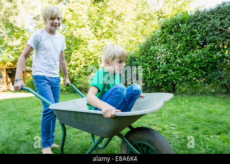 Due fratelli giocare con la carriola in giardino Foto Stock