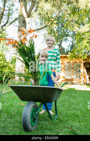 Due fratelli giocare con la carriola in giardino Foto Stock