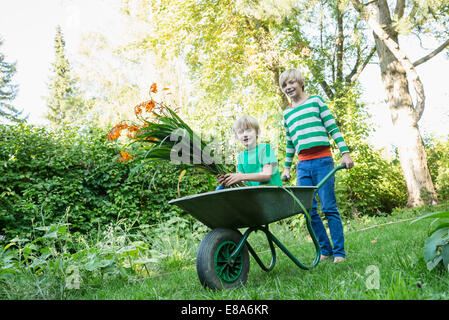 Due fratelli giocare con la carriola in giardino Foto Stock