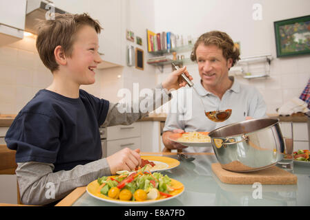 Padre e figlio di mangiare gli spaghetti e insalata in cucina Foto Stock