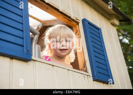 Sorridente bambina guardando fuori di casa ad albero Foto Stock