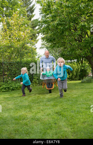 Padre nel giardino spingendo i bambini in carriola Foto Stock