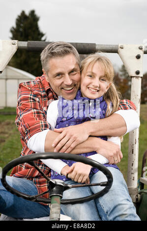 Agricoltore abbracciando la figlia sul trattore Foto Stock