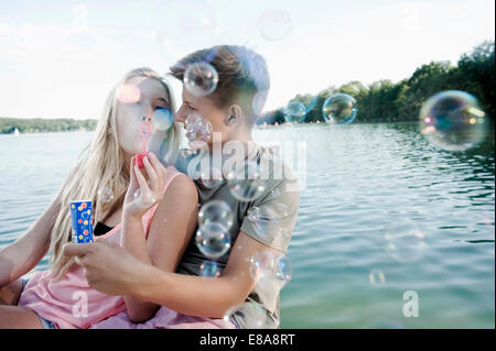 Giovane adolescente soffiando bolle di sapone su un molo al lago Foto Stock