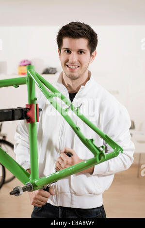 Giovane uomo che lavora sul telaio di bicicletta, sorridente, ritratto Foto Stock