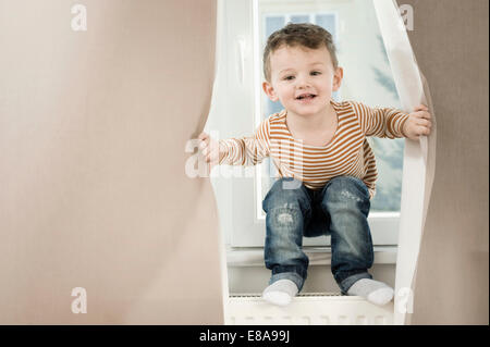 Ritratto di ragazzo giocando con tendina, sorridente Foto Stock