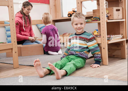 Piccolo Ragazzo seduto per terra nel suo kindergarten Foto Stock
