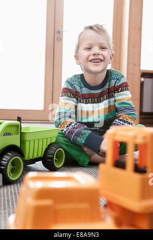 Ritratto di sorridere piccolo ragazzo seduto sul suolo del suo kindergarten Foto Stock