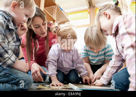 Educatore femmina e quattro bambini guardando picture book Foto Stock