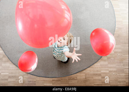 Little Boy giocando con palloncini rossi in asilo nido, vista in elevazione Foto Stock