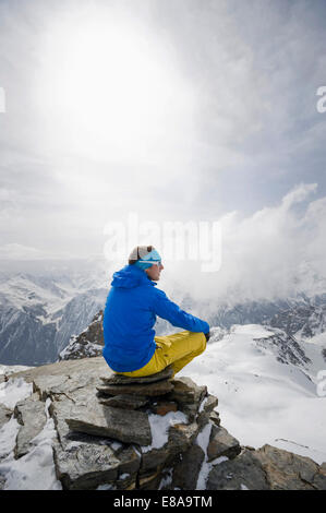 Uomo seduto contemplando la montagna invernale di picco Foto Stock