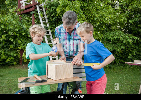 Padre ragazzi costruire birdhouse garden la perforazione Foto Stock