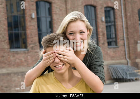 Ritratto di ragazza adolescente che copre gli occhi del ragazzo adolescente, sorridente Foto Stock