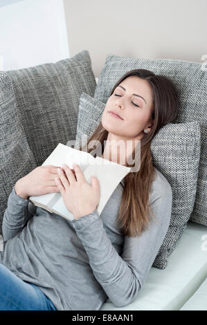 Ritratto di giovane donna con libro aperto che dorme sul divano di casa Foto Stock