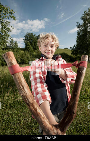 Giovane ragazzo biondo holding slingshot in legno Foto Stock