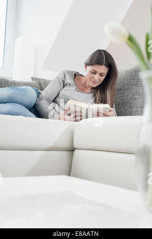 Giovane donna la lettura di un libro sul suo lettino a casa Foto Stock