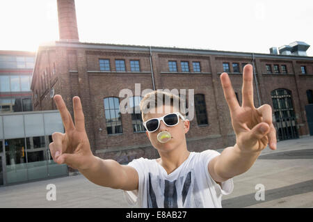 Ragazzo adolescente soffiando bubble gum e che mostra segni di pace Foto Stock