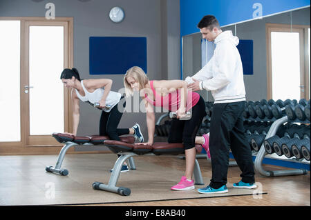 Coach di supporto di due donne in palestra facendo il peso della formazione Foto Stock
