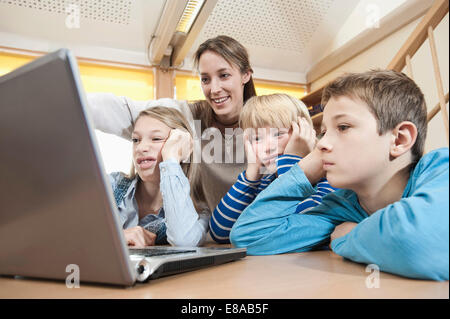 Femmina assistente di puericultura e tre bambini di trivellazione guardando al laptop Foto Stock